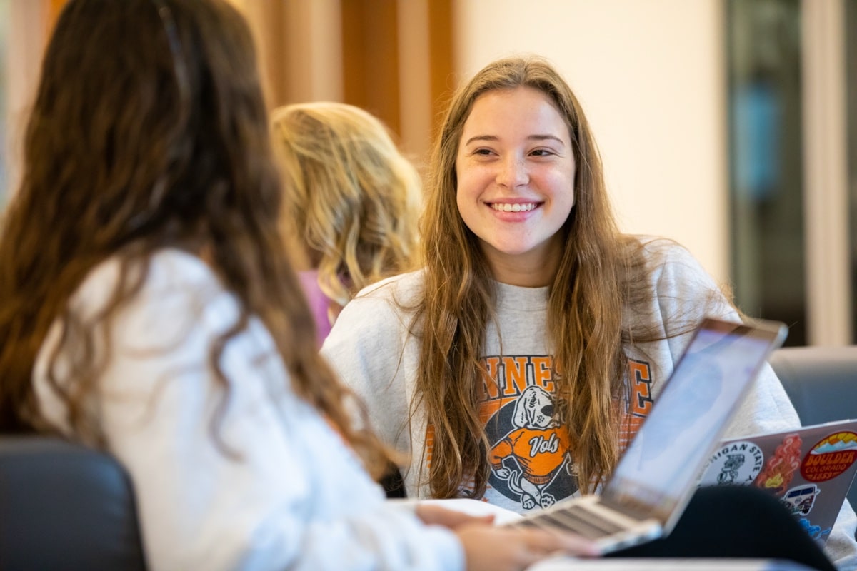 A UT student smiles while talking with peers over laptops in a campus lounge