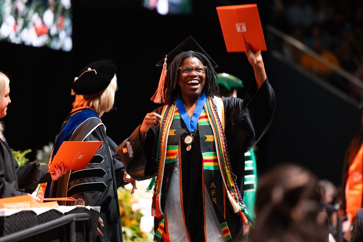A UT graduate celebrates on stage holding a diploma at commencement