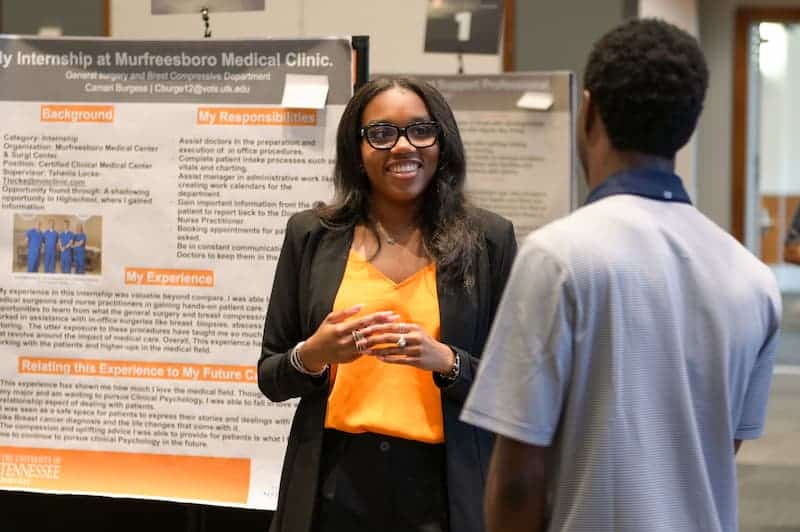 Student talking with a visitor in front of her internship research poster at a showcase