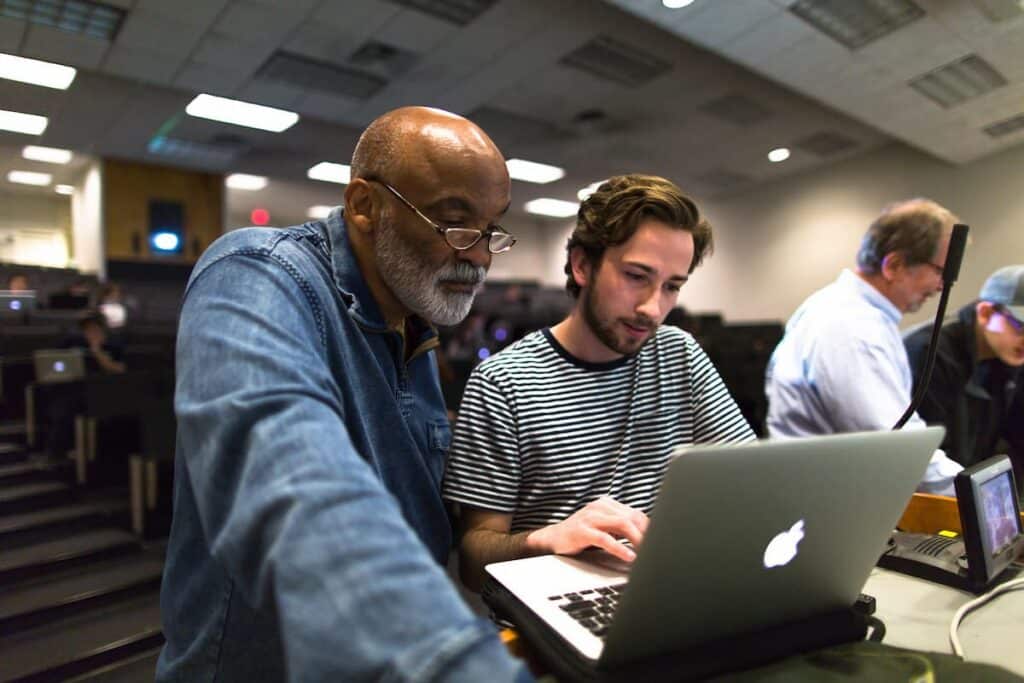 Instructor leaning in to help a student working on a laptop in a tiered lecture hall