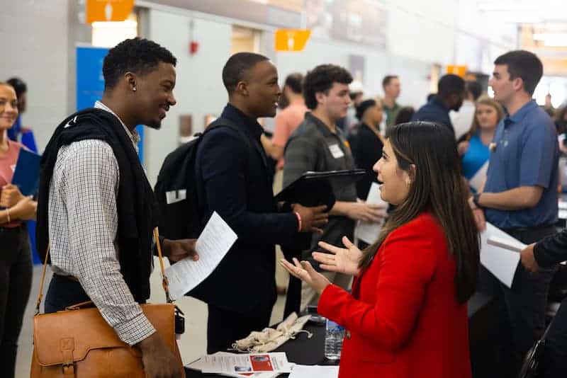 Student with a leather messenger bag talking with a recruiter in a red blazer at a job fair