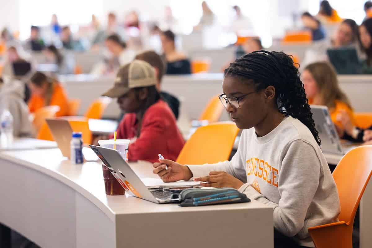 Student in a Tennessee sweatshirt taking notes on a laptop in a large tiered classroom