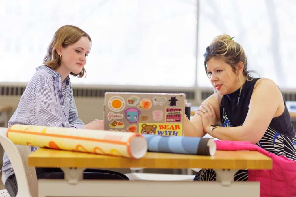 Two people discussing work on a laptop, with rolled drawings on the table beside them