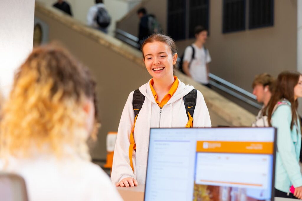 Student smiling while talking with a staff member across a campus service desk