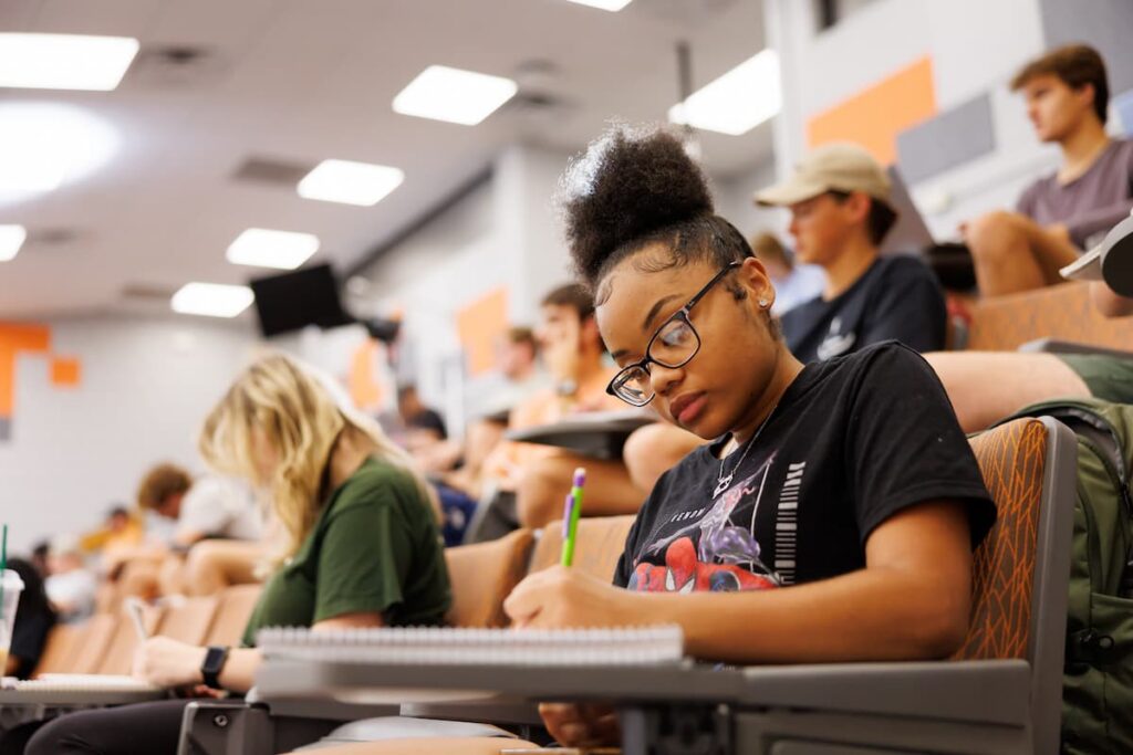 Student taking notes in a spiral notebook during class in a tiered lecture hall