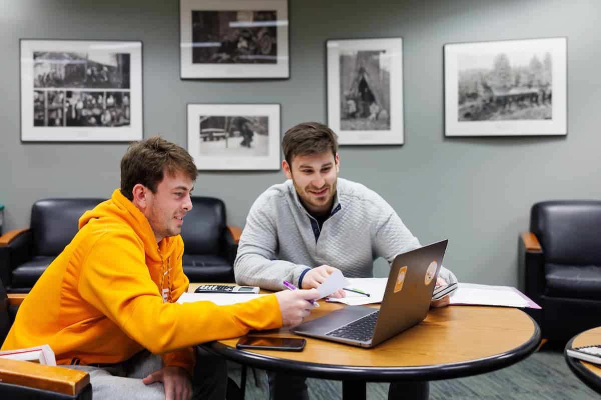 Two students reviewing work together on a laptop at a small table in an office