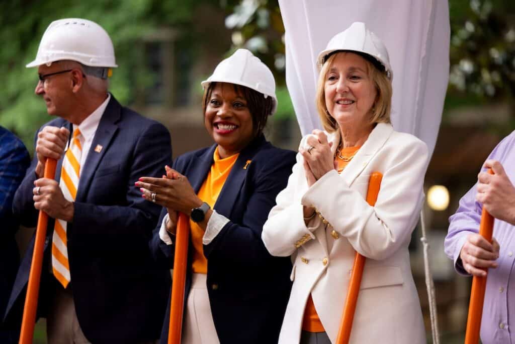 University leaders in hard hats holding orange shovels at a groundbreaking ceremony
