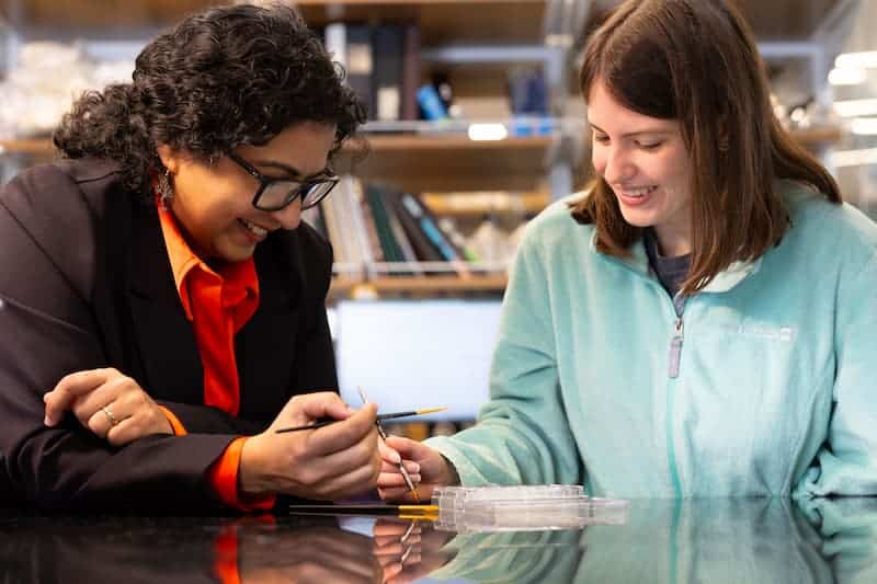 Faculty member and student examine a specimen with fine tweezers at a lab bench