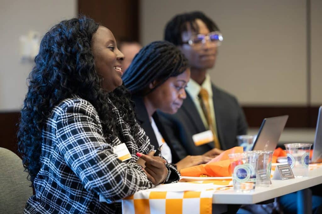 Panelists in business attire smile and take notes at a table during a career panel discussion