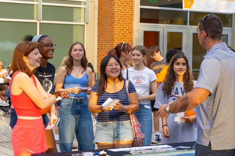 Students gathered around an outdoor information table talking with a staff member